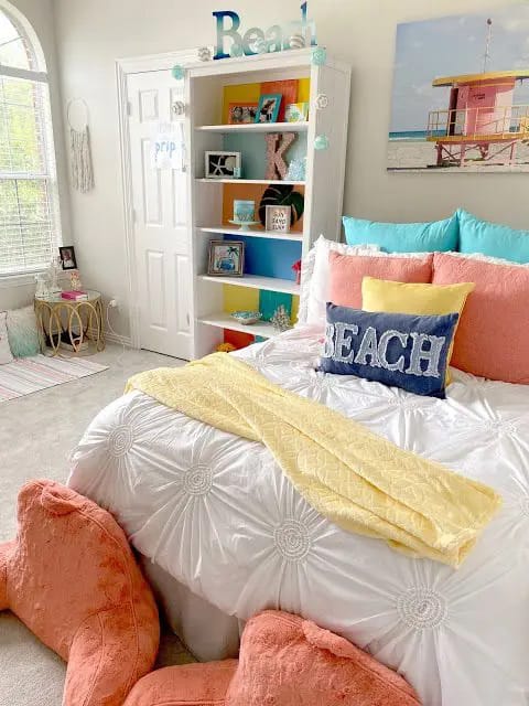 Beach-themed teen bedroom with pastel pillows, a colorful bookshelf, and beach-inspired decor.