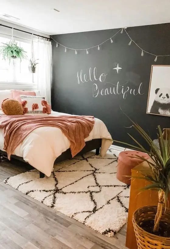 Teen bedroom with a black chalkboard wall, pink bedding, and a fluffy rug.