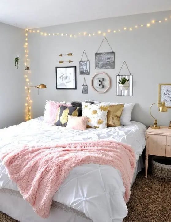 Teen bedroom with pink and gold decor, featuring fairy lights and wall art.