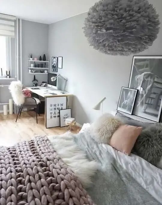 Cozy gray room with a chunky knit blanket, fluffy pillows, and a feathered light fixture.