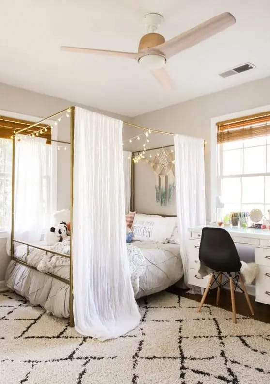 Canopy bed with string lights, sheer curtains, and a modern workspace.