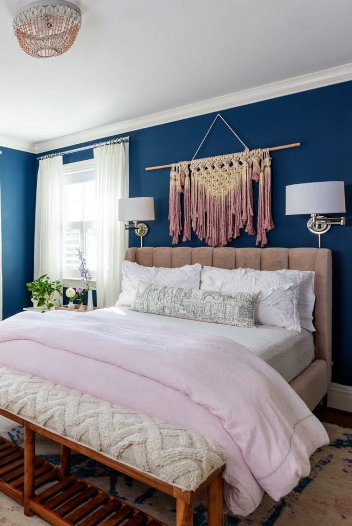 Boho-chic room with deep blue walls, macramé wall hanging, and pink bedding.