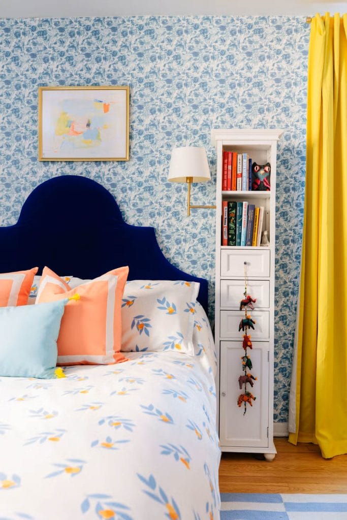 Bright and cheerful room with floral patterns, bold colors, and a deep blue headboard.