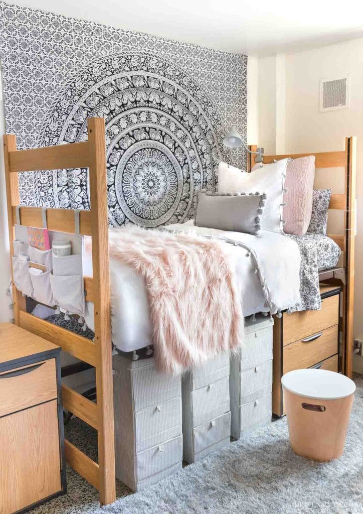 A dorm room with a bed, mandala tapestry on the wall, cozy bedding, and various storage solutions.