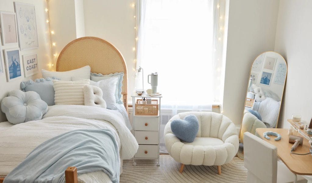 Room with a blue and white color palette, cozy bed, plush pillows, and a heart-shaped chair.