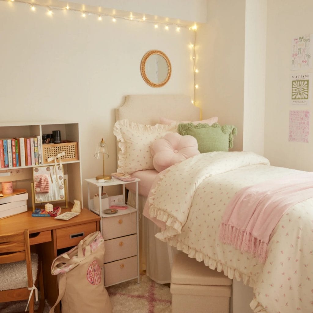 Cozy dorm room with pastel floral bedding, pink and green pillows, string lights, and a functional study desk.