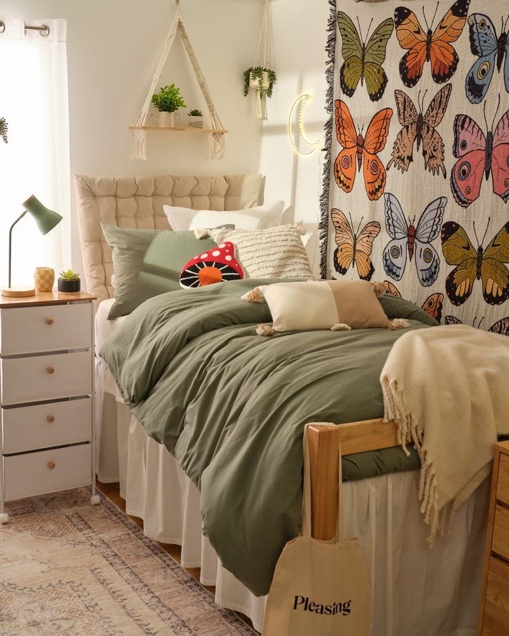 A cozy dorm room with green bedding, butterfly tapestry, hanging plants, and soft textures.