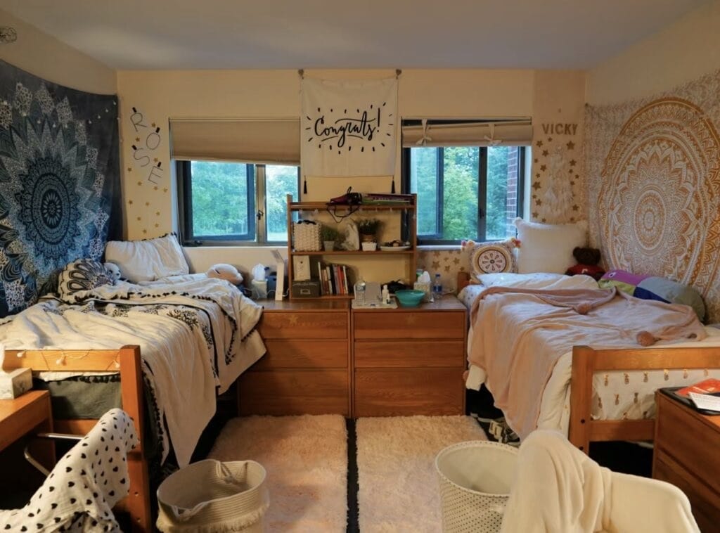 A shared dorm room with boho tapestry wall hangings, warm lighting, and cozy bedding.