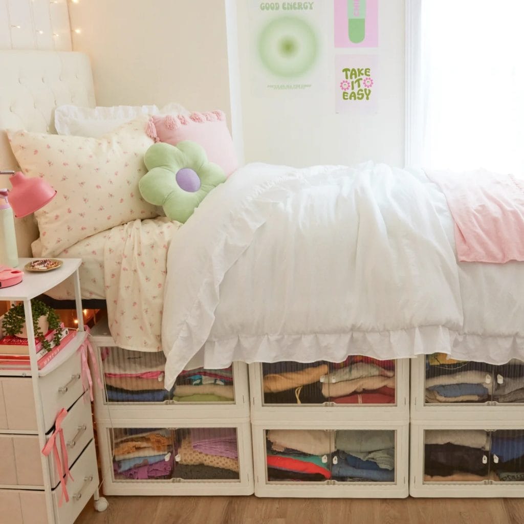 A bed with pastel-colored bedding and a floral pillow, with organized under-bed storage boxes.