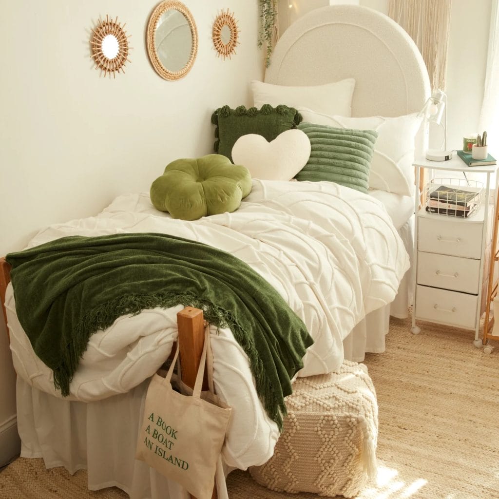 Dorm room with a green and white bedding theme, decorative throw pillows, round mirrors, and leafy garlands.