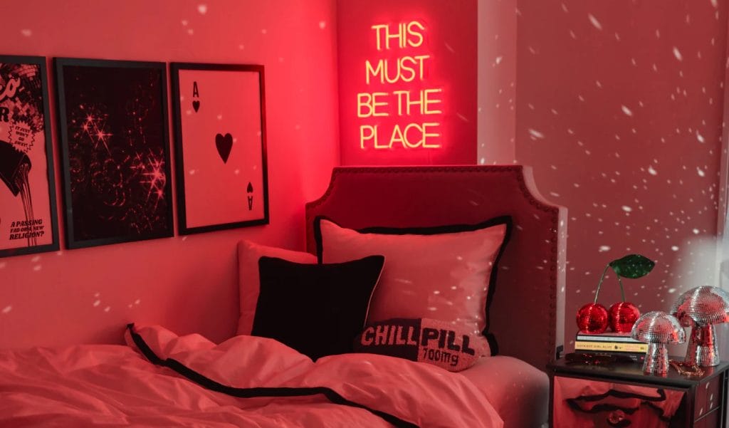 A room with a red and black color scheme, neon sign, framed wall art, and a bed with contrasting pillows.