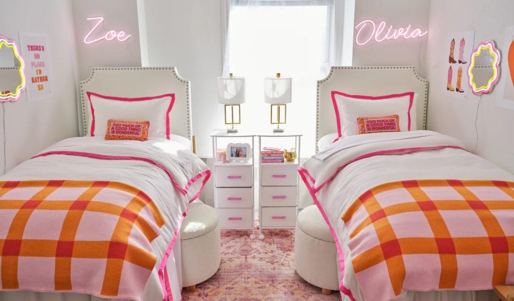 A room with twin beds, white and pink bedding, neon name signs, and matching nightstands.