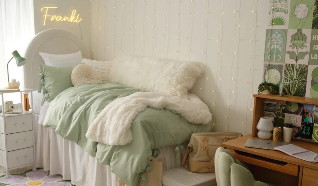 A serene room with a white bed, green bedding, string lights, a personalized neon sign, and a small desk area.