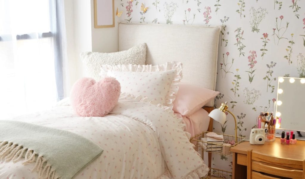 A room with soft pink bedding, a heart-shaped pillow, and floral wallpaper for a charming and delicate look.