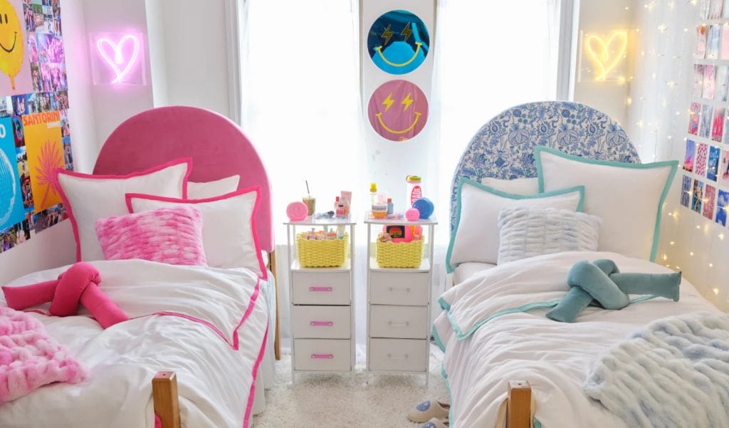 A room with twin beds, pink and blue bedding, colorful wall art, and a neon sign for a fun and lively look.