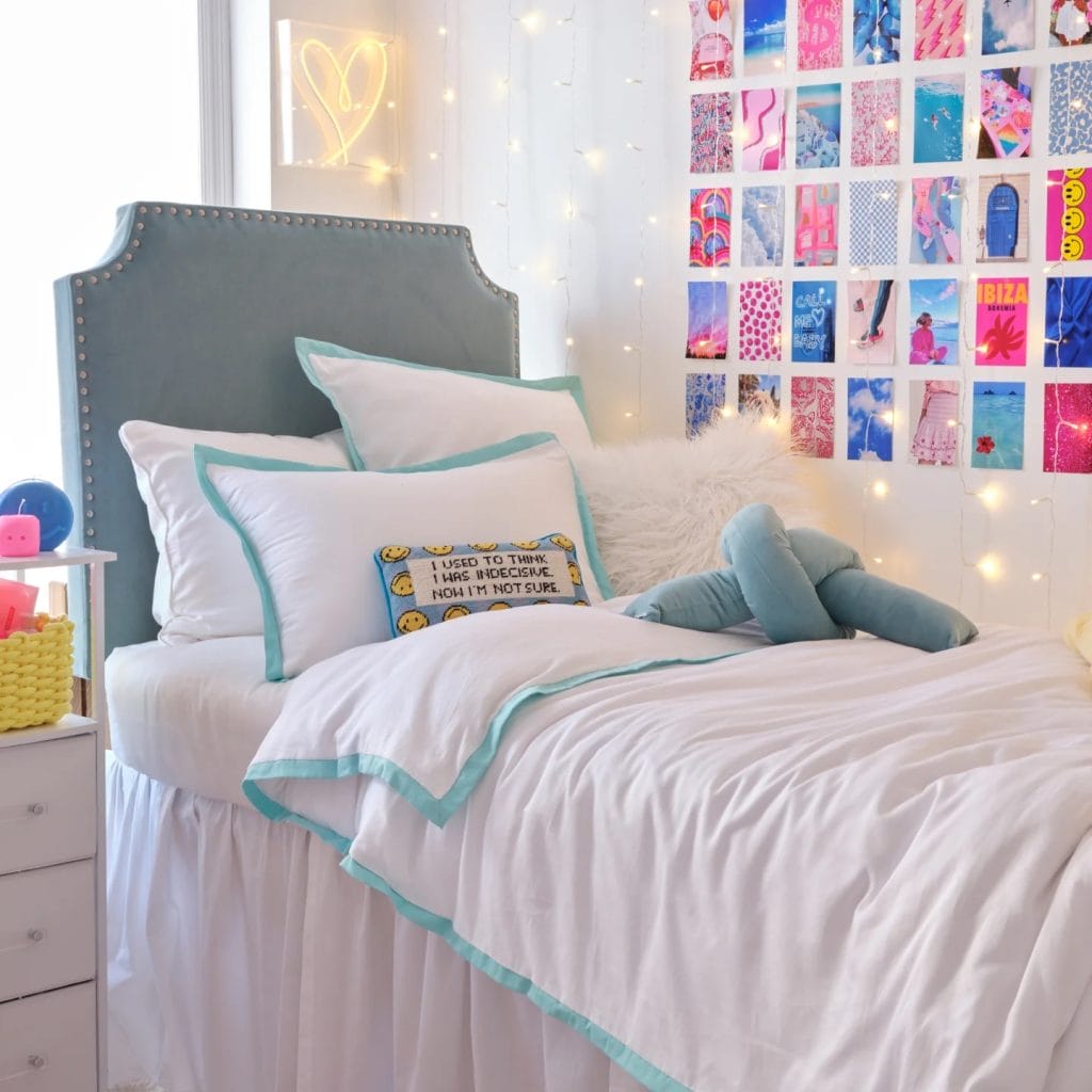 A cozy room with white and blue bedding, fairy lights, and a colorful photo wall for a cheerful and inviting atmosphere