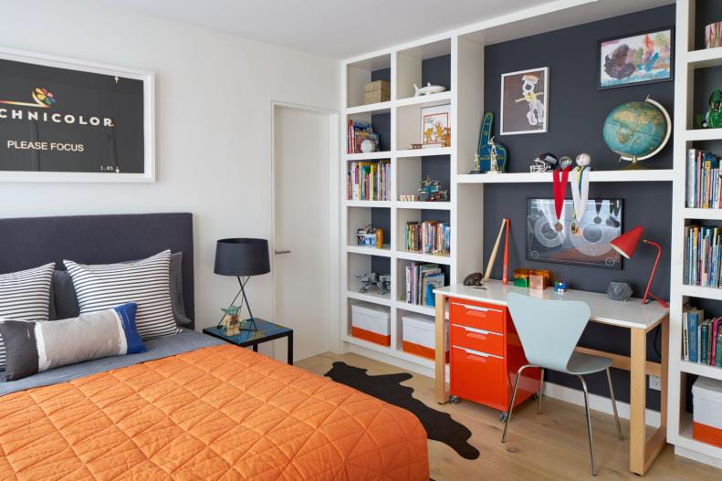 Teen boy's room with a bright orange desk, built-in shelves, and a stylish bed.