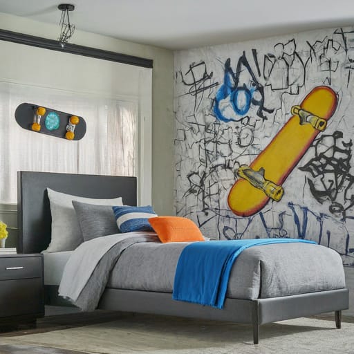 A bedroom with a graffiti mural featuring a skateboard, gray bedding with orange and blue accents, and a modern bed frame.