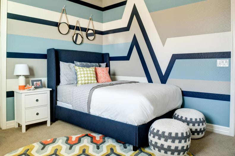 Teen boy's room with a geometric wall design in blue and gray, simple furniture, and colorful accents.