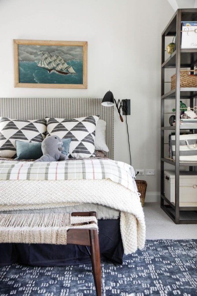 Teen boy's room with nautical decor, a ship painting, and cozy, patterned pillows.