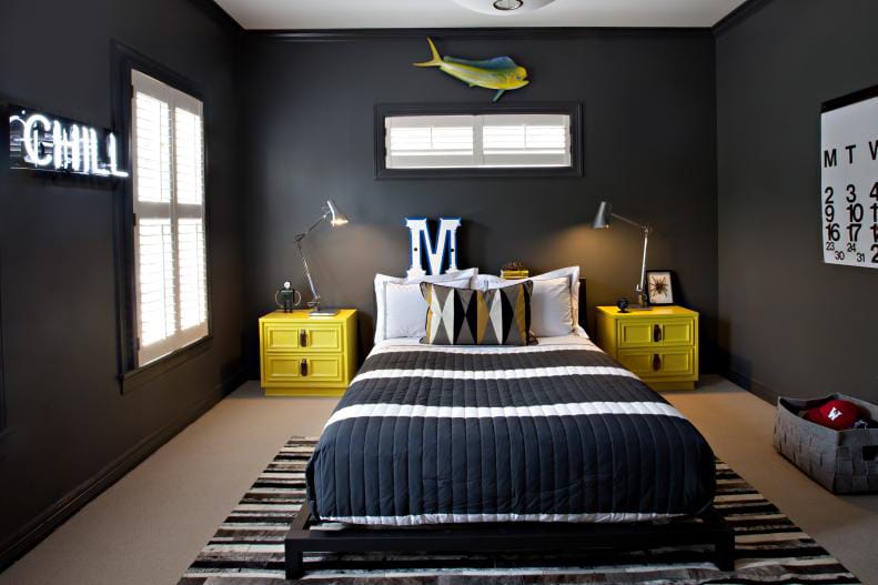 Teen boy's room with dark walls, yellow side tables, and modern decor elements like a neon "Chill" sign.