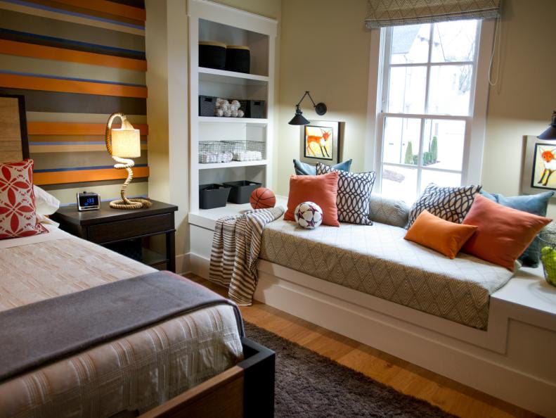 Teen boy's room with a built-in window seat, striped accent wall, and warm color palette.