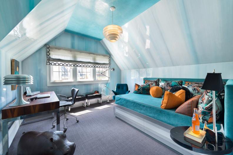 Blue-themed attic room with a large daybed, patterned pillows, and a modern desk setup.