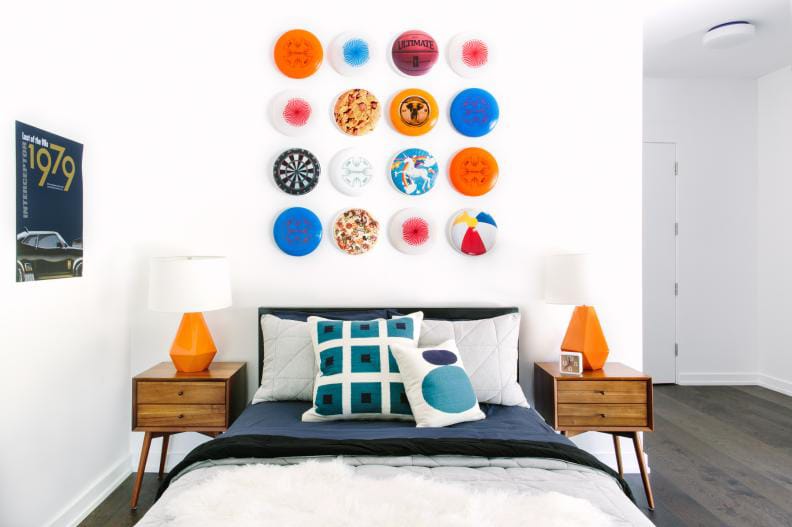 Room with a wall display of colorful frisbees, mid-century modern side tables, and orange lamps.