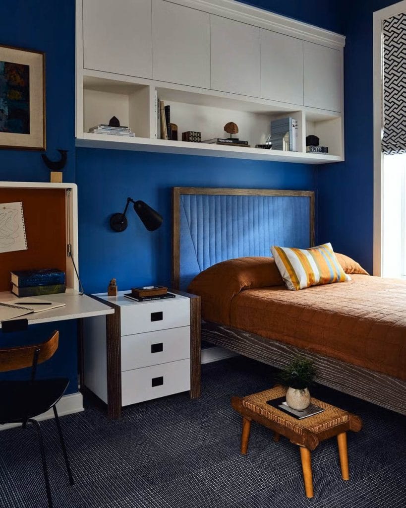 Teen boy's bedroom with bold blue walls, brown bedding, and a built-in study area.