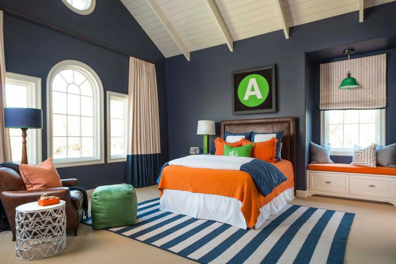 A spacious teen boy's bedroom with high ceilings, navy walls, and orange accents.