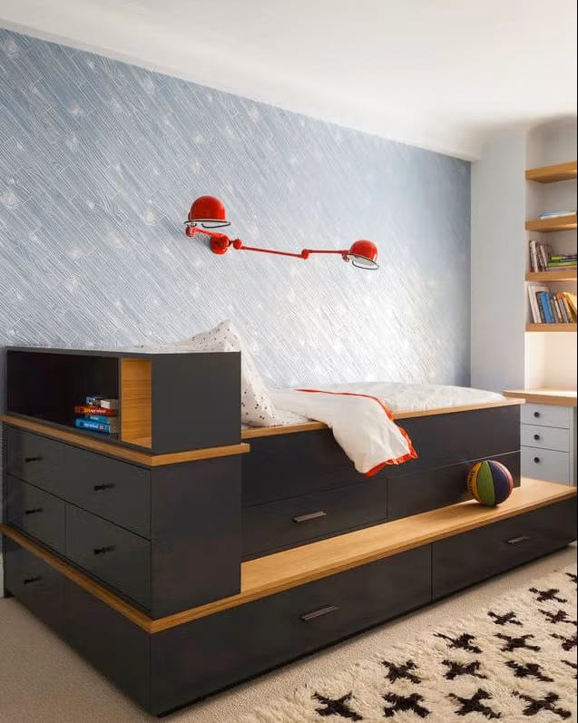 Teen boy's bedroom with a bed featuring built-in storage drawers, a red wall lamp, and minimalist decor.