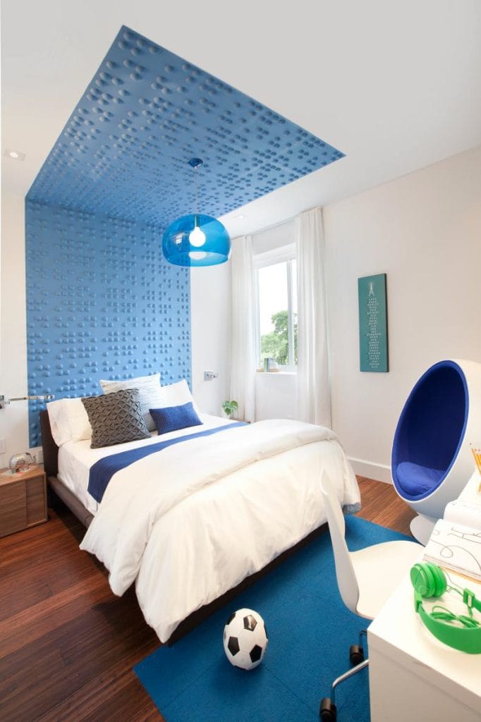 A modern blue and white teen bedroom with a textured blue wall and ceiling, a white desk, and a blue pod chair.