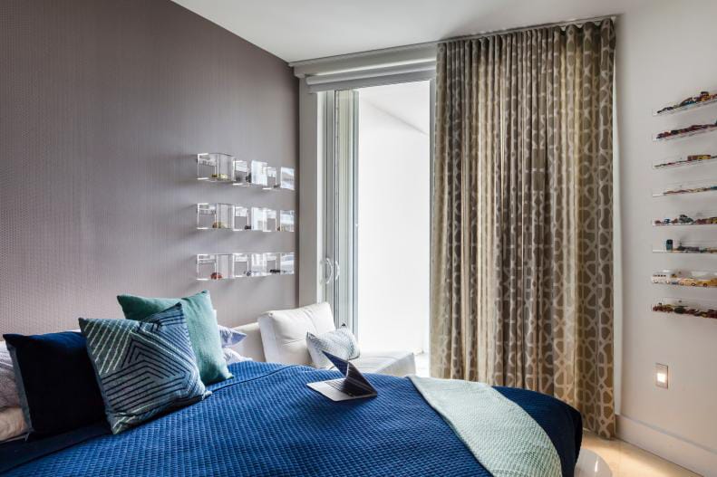 A modern teen boy's bedroom with blue and gray decor, a wall of model cars, and minimalist furniture.