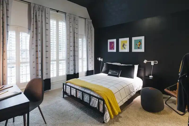 A modern bedroom with black walls, a yellow throw blanket, and minimalistic decor.