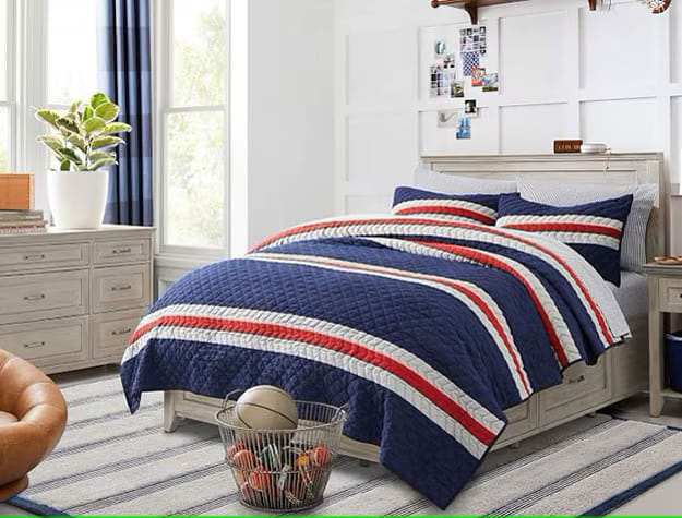 A bedroom with striped bedding in navy, red, and white, with large windows allowing natural light.