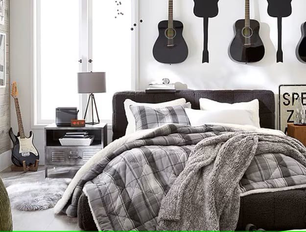 A bedroom with guitars hung on the wall above the bed and cozy gray bedding.