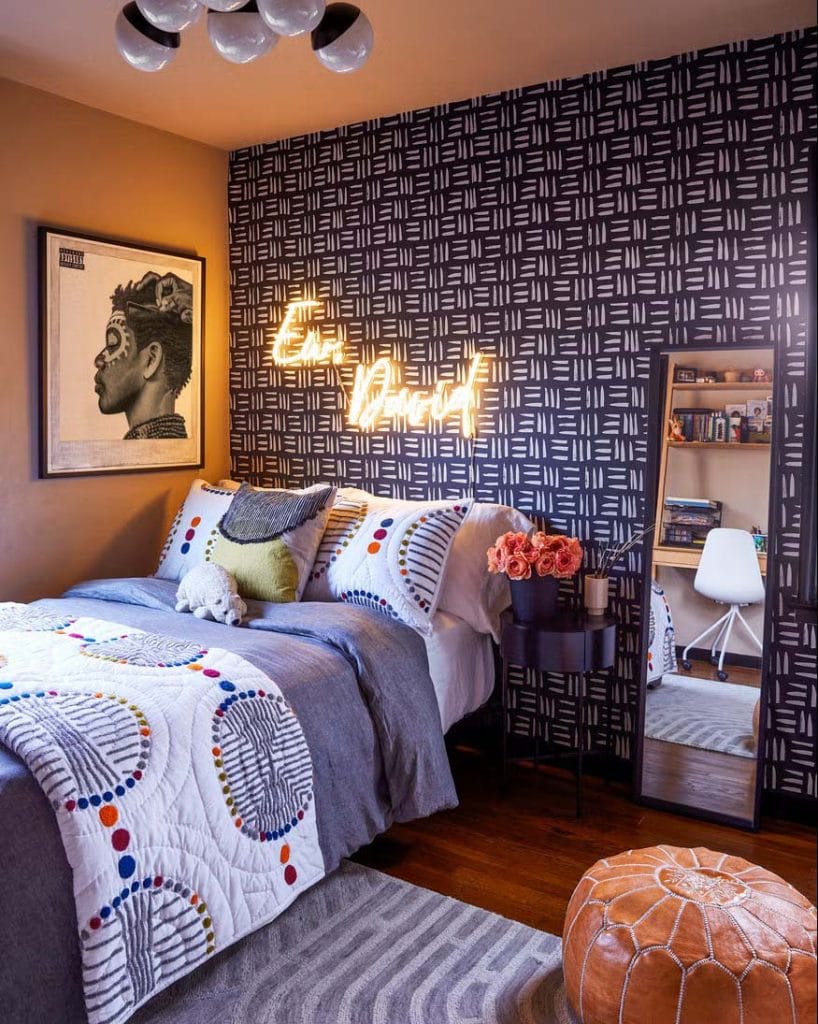 Teen boy's bedroom with a black and white patterned wall, neon sign, and colorful bedding.