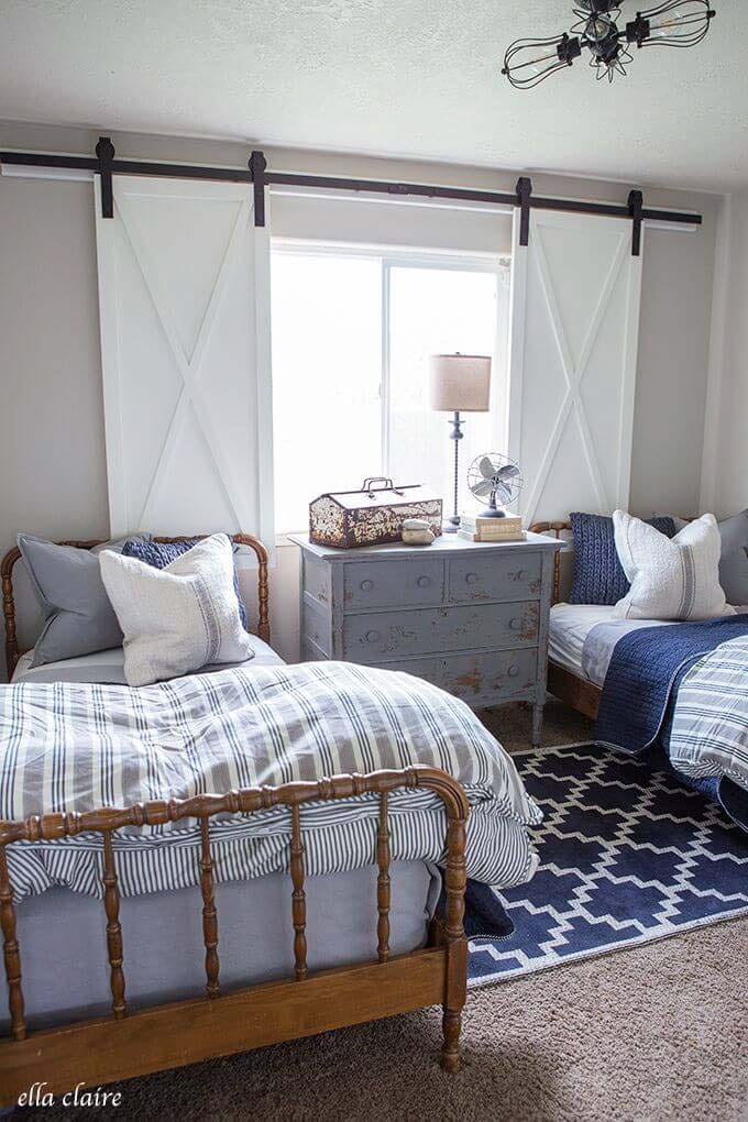 Twin beds with wooden frames and a vintage dresser, with white barn doors in the background.