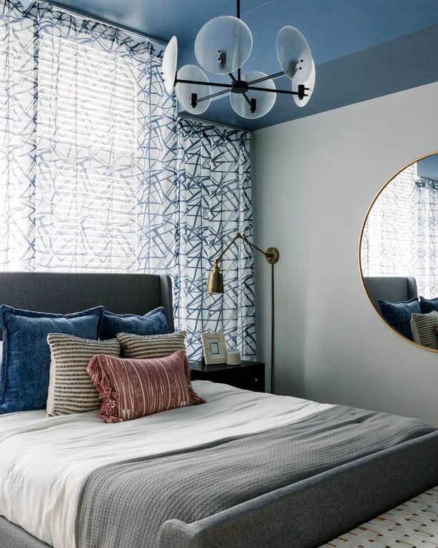 Teen boy's bedroom with a blue ceiling, gray walls, and modern decor elements like a round mirror and abstract curtains.