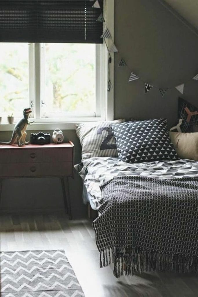 A cozy bed with geometric patterned bedding and a small dinosaur figure on the nightstand.