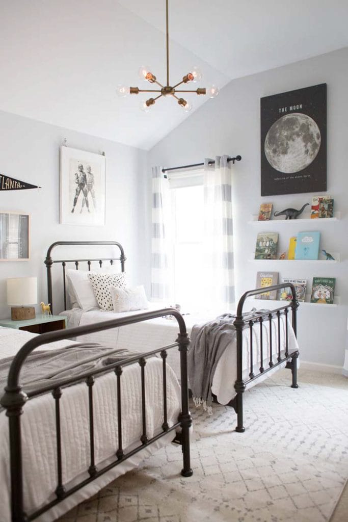 A bright and airy room with twin metal-framed beds, modern chandelier, and neutral bedding.