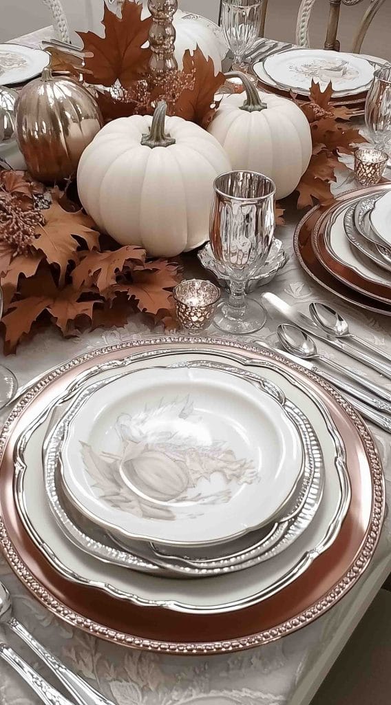 Elegant table setting with layered plates, white pumpkins, and autumn leaves.