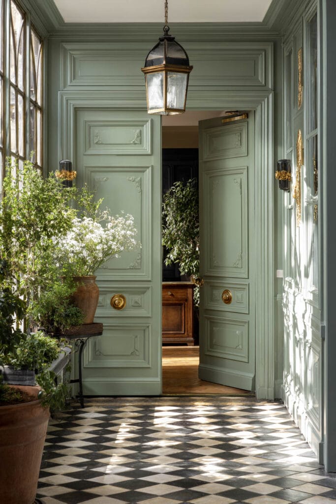 Sage green entryway with ornate double doors, checkerboard floors, gold hardware, and potted greenery.