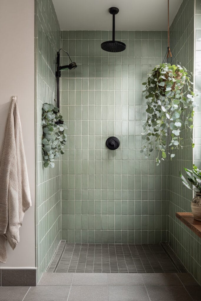 Sage green shower with black fixtures, hanging greenery, and spa-inspired modern design.