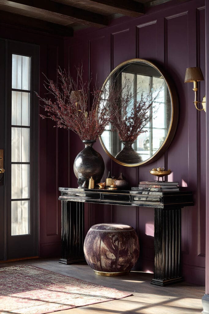 Bold entryway with plum walls, black console, round mirror, and brass accents in moody lighting.