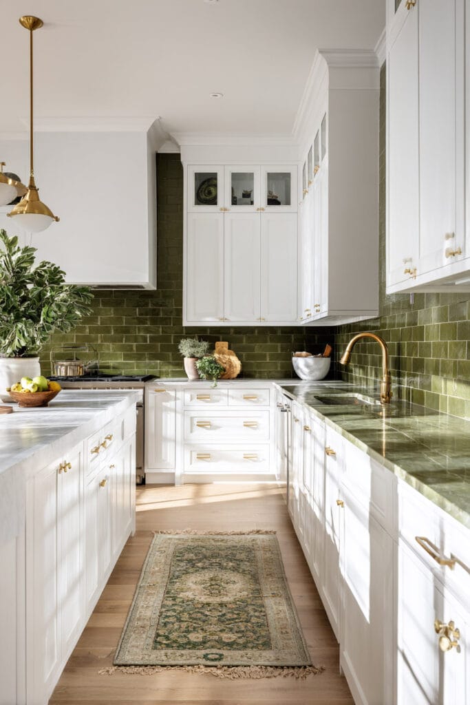 White kitchen with olive green backsplash and countertops, brass hardware, and a vintage runner rug. Warm light, natural textures, and earthy color palette create a modern organic kitchen design.