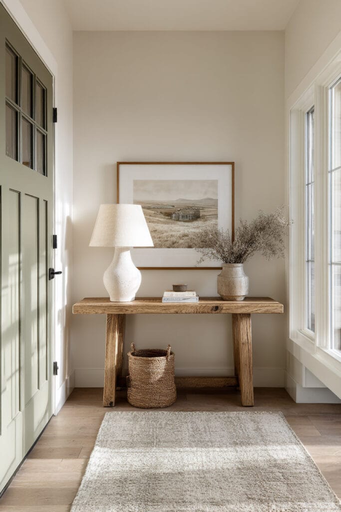 Neutral entryway with sage green front door, wooden console table, ceramic lamp, and natural decor creating a warm and inviting earthy color palette.