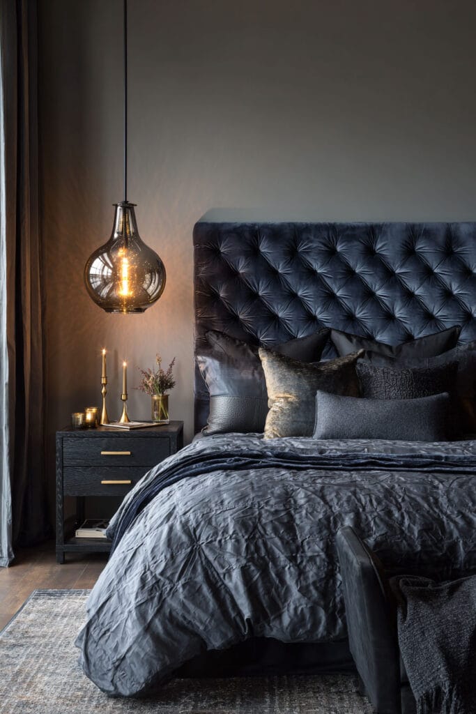 Moody bedroom with navy velvet headboard, dark bedding, and pendant light with brass accents.