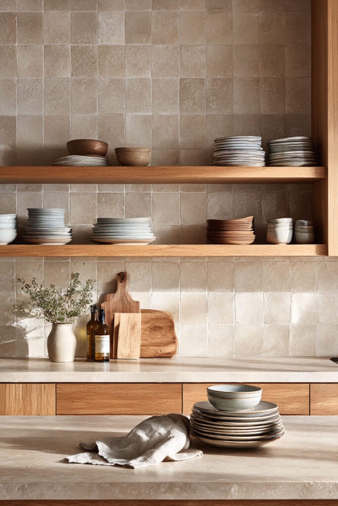 minimal kitchen backsplash with neutral tile, open wood shelving, and stacked dishes in a warm organic modern kitchen design