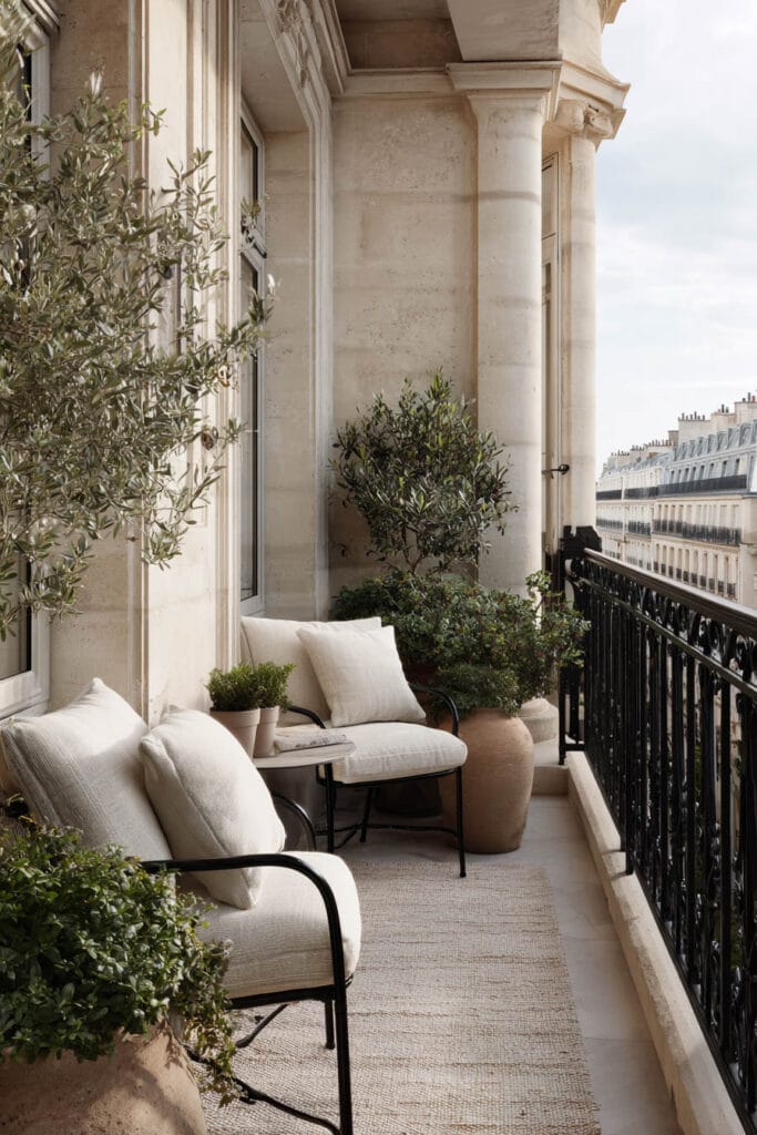 French balcony with neutral cushions, black wrought iron railing, stone architecture, olive trees, and timeless Parisian outdoor decor.